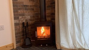 A wood-burning stove in a corner with a brick wall and a curtain. - The Barn - Farm Stay (Shepshed)