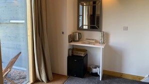 A small, well-lit room with a white wardrobe, a mirror, a shelf with a kettle, a basket, and a trash bin. - The Barn - Farm Stay (Shepshed)