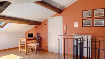 A room with a sloped ceiling, wooden beams, a desk with a chair, a laptop, and framed pictures on the wall.
