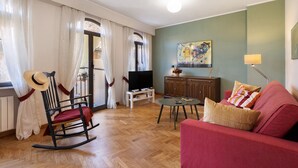 Een woonkamer met een schommelstoel, een rode bank, een televisie en een kast.
