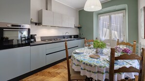 Een moderne keuken met grijze kastjes, een inbouwoven en een eethoek met een tafel gedekt voor twee personen.