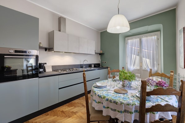 Une cuisine moderne avec des meubles gris, un four encastré et un coin repas avec une table dressée pour deux personnes.