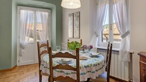 Een eetruimte met een tafel gedekt voor twee personen, stoelen, een hanglamp en uitzicht door het raam.
