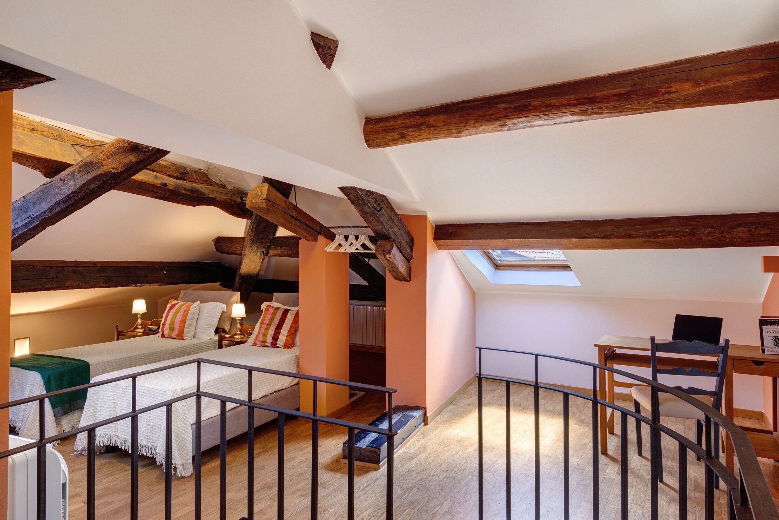 Une chambre à coucher aménagée dans un espace de type « loft », avec des poutres en bois apparentes, une lucarne, un bureau et une chaise.