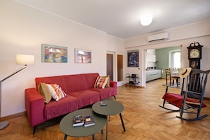 Un salon avec un canapé rouge, deux petites tables, un lampadaire et un fauteuil à bascule.