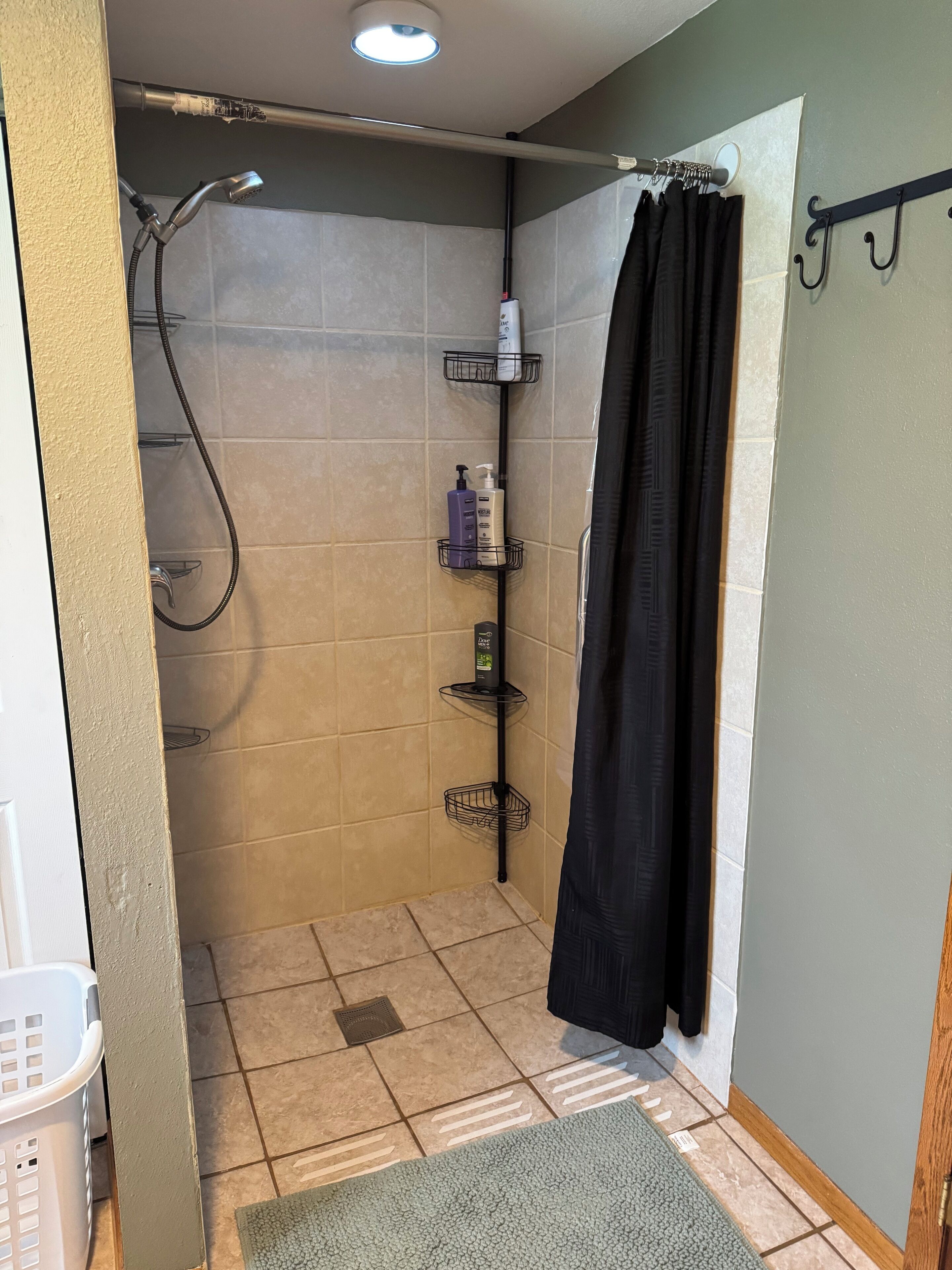 Un petit espace de douche carrelé, équipé d’un pommeau de douche, d’un porte-serviettes et d’une étagère pour les articles de toilette.