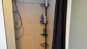 Un petit espace de douche carrelé, équipé d’un pommeau de douche, d’un porte-serviettes et d’une étagère pour les articles de toilette.
