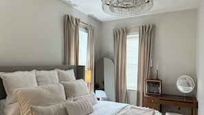 Ein Schlafzimmer mit einem großen Bett, einem Holztisch, einem runden Spiegel und einer Chandelier.