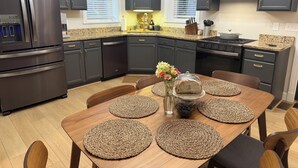 Eine moderne Küche mit dunklen Schränken, einem Edelstahl-Kühlschrank und einem Essbereich mit Holztisch und gewebten Tischsets.