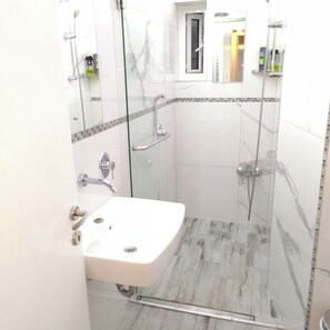 Une salle de bain moderne avec une douche à parois de verre, un lavabo blanc et un carrelage au sol.