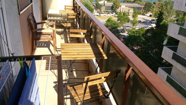 A balcony with wooden furniture, a clothes rack, and a view of the sea and buildings. - Apartment - Sleeps 5 - Parking - Balcony (Thessaloniki)