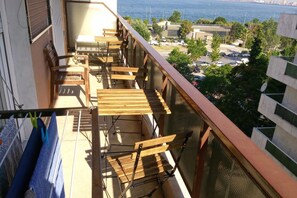 Een balkon met houten meubels, een kledingrek en uitzicht op zee en gebouwen.
