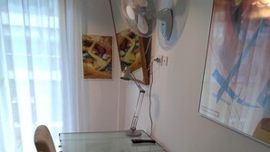 A room with a desk, a standing fan, a painting, and a window with curtains. - Apartment - Sleeps 5 - Parking - Balcony (Thessaloniki)
