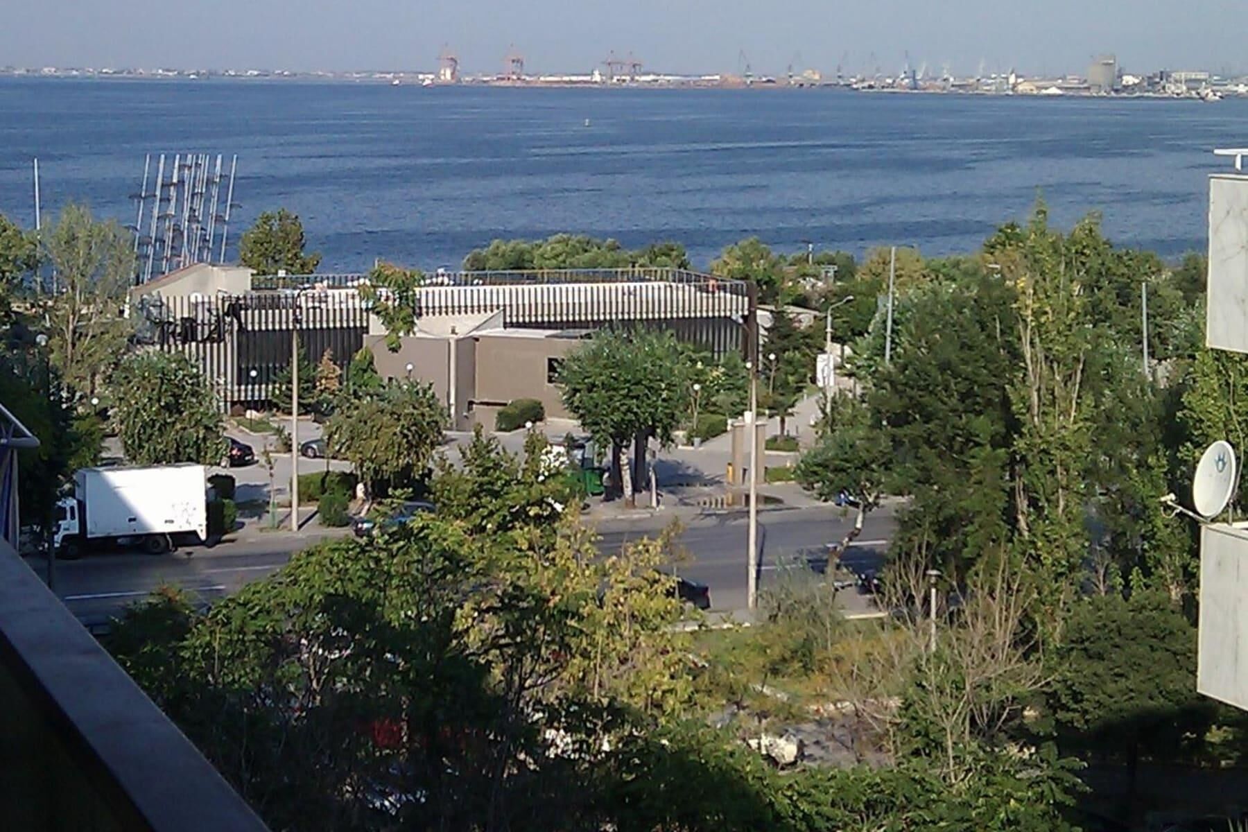 A coastal view with a modern building featuring a curved roof and a parking area.