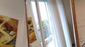 A room with a large mirror reflecting a window and a balcony. There is a painting on the wall. - Apartment - Sleeps 5 - Parking - Balcony (Thessaloniki)