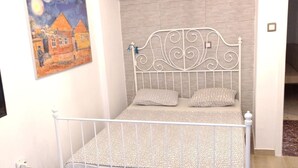 A bedroom with a metal bed frame, two pillows, and a painting on the wall. - Apartment - Sleeps 5 - Parking - Balcony (Thessaloniki)