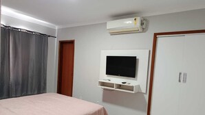 Een slaapkamer met een bed, een aan de muur bevestigde televisie, een airconditioner en een kledingkast.