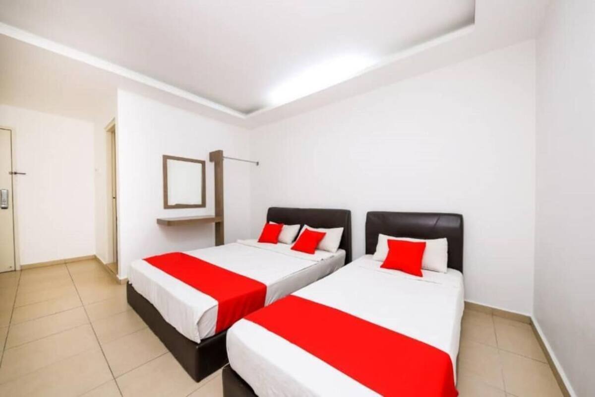A hotel room with two beds, each with white bedding and red accents, a small bedside table, and a wall-mounted mirror.