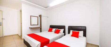 A hotel room with two beds, each with white bedding and red accents, a small bedside table, and a wall-mounted mirror.