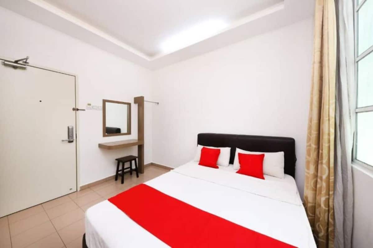 A bedroom with a bed, a mirror, a small stool, and a door.