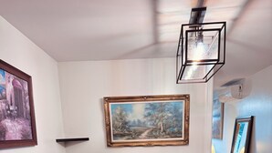 A dining area with a long wooden table, dark upholstered chairs, a painting on the wall, and a hanging light fixture.