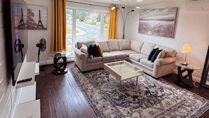A modern living room with a sectional sofa, a glass coffee table, and a large window with curtains.