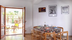 Een eetgedeelte met een tafel voor vier personen, omringd door houten stoelen met geweven zittingen. Een glazen deur leidt naar een buitengebied met een bamboescherm.