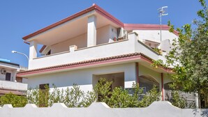 Een tweelaags huis met een balkon, een zichtbare airconditioning en een kleine tuin aan de voorkant.