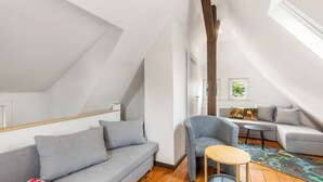 A loft-style room with a sloped ceiling, a gray sofa, a gray armchair, a small round table, and a colorful rug. - Holiday Home 'Feußner' with Wi-Fi (Schwalmtal)