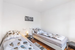 Une chambre avec deux lits, une table de chevet avec une lampe, une petite table et un tableau accroché au mur.