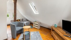 A modern living room with a loft bed, a grey armchair, a wooden coffee table, a TV stand, and a bookshelf. - Holiday Home 'Feußner' with Wi-Fi (Schwalmtal)