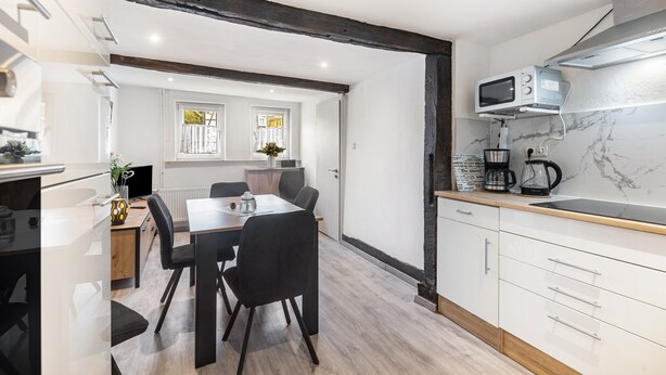 A modern kitchen with white cabinetry, a wooden dining table, and a built-in microwave. - Holiday Home 'Feußner' with Wi-Fi (Schwalmtal)