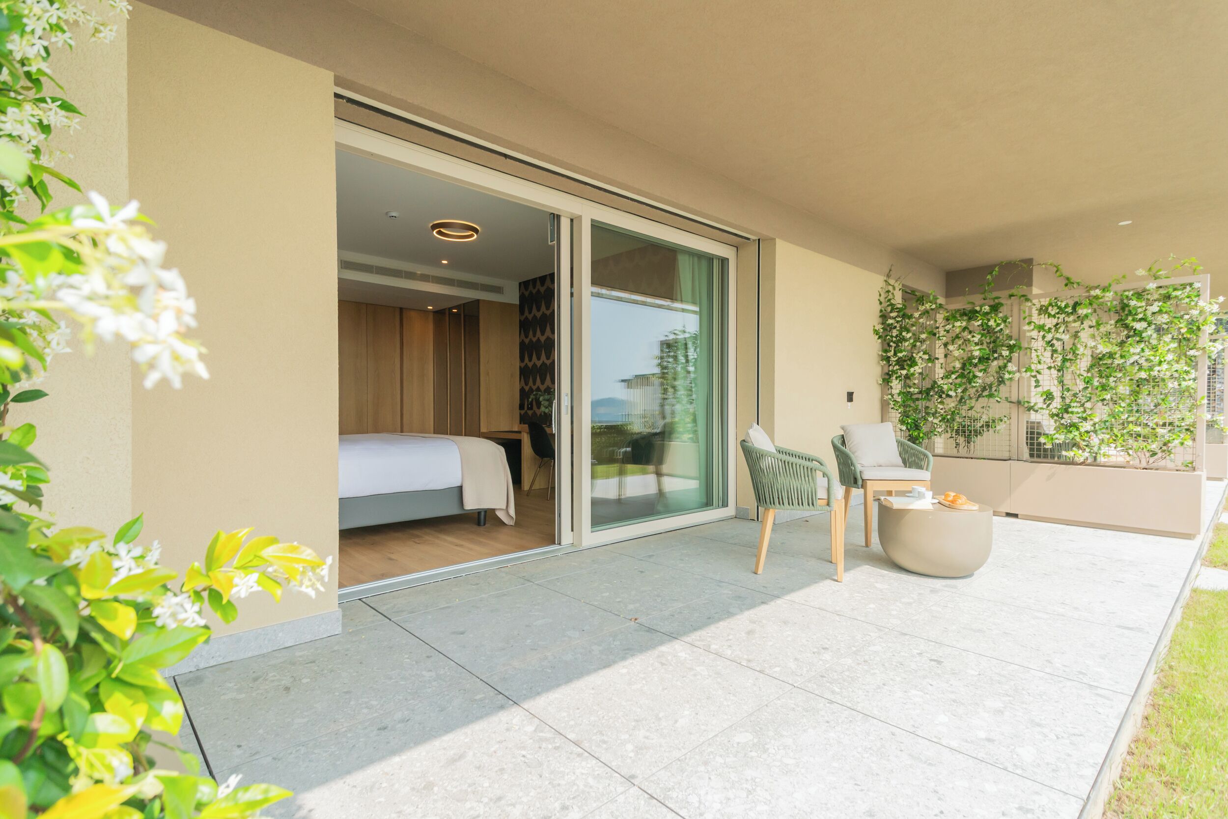 A modern hotel room with a sliding glass door leading to a balcony, a green chair, and a round coffee table.