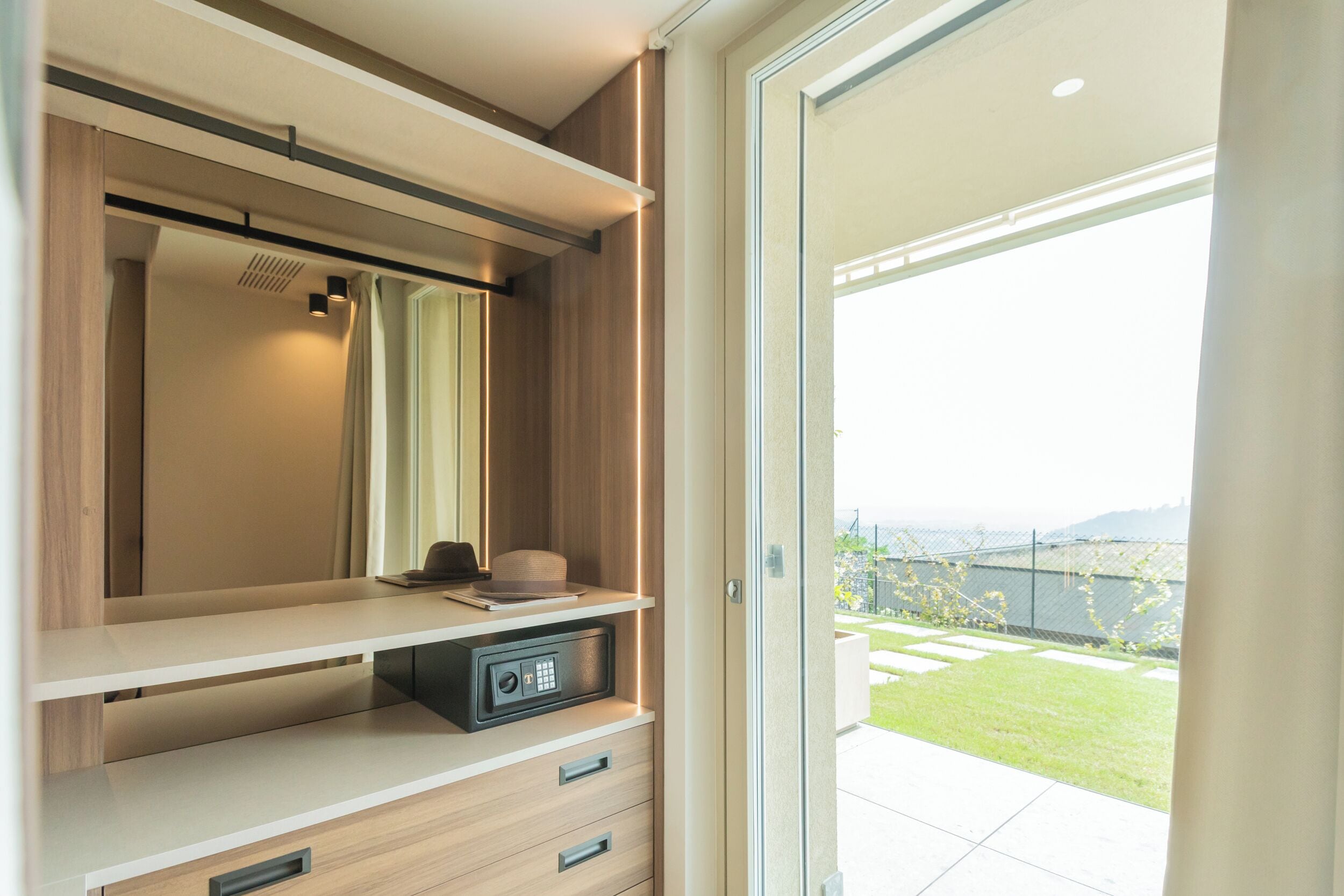 Ein modernes Zimmer mit einer Schiebeglasdoor zum Balkon, einem fest eingebauten Safe und einem minimalistischen Design.