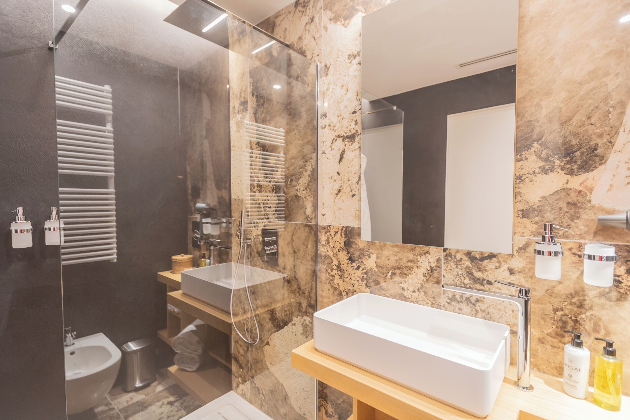 Ein modernes Badezimmer mit Duschkabine aus Glas, einem weißen Waschbecken und einer Wand mit Marmorfliesen.
