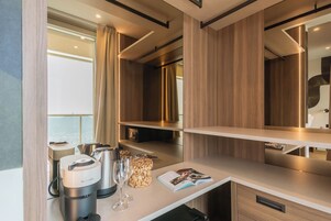 Habitación de hotel moderna con minibar, cafetera, una copa de vino y una revista sobre la encimera.
