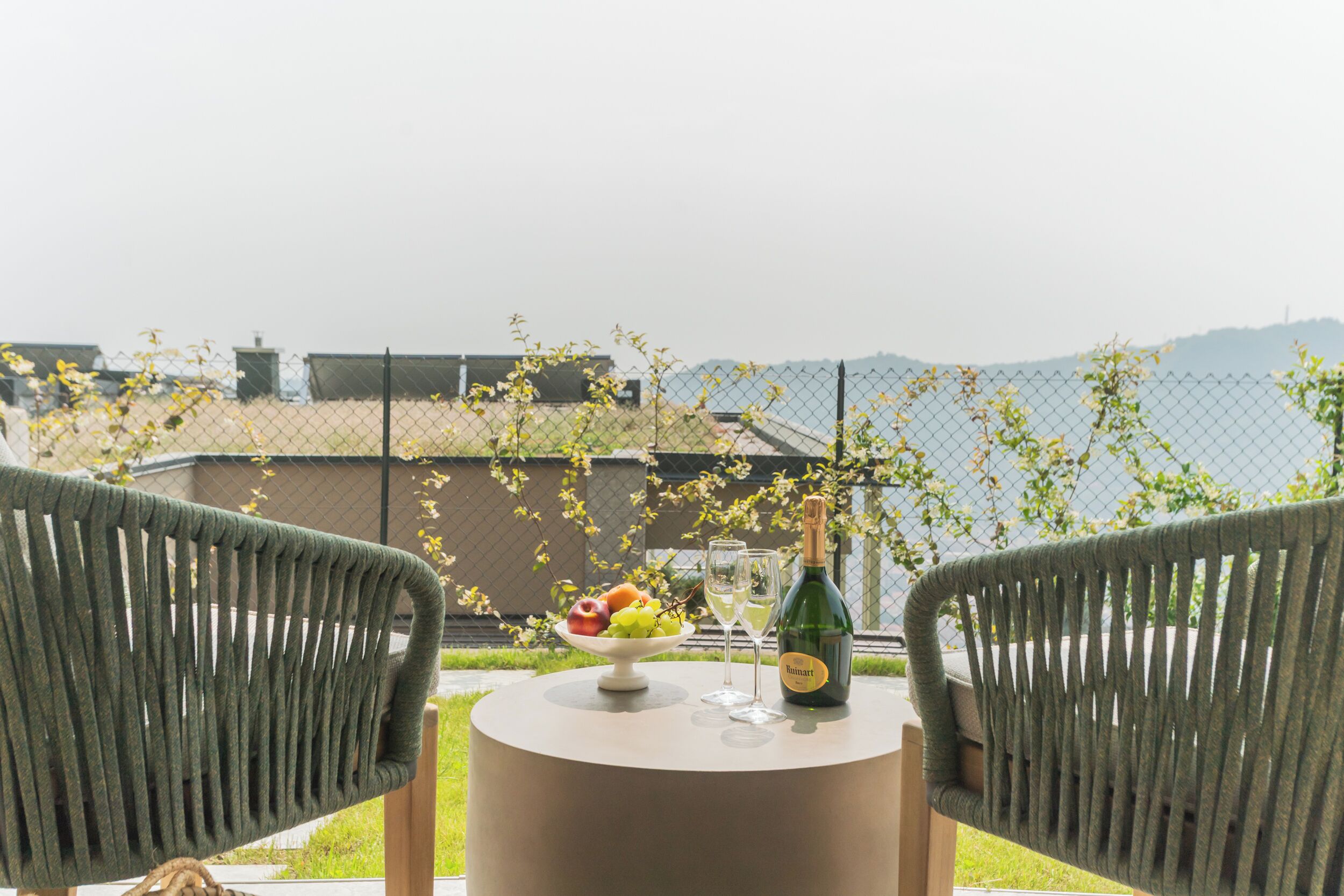 A balcony with wicker chairs, a table with a bottle of wine, glasses, and a fruit bowl.