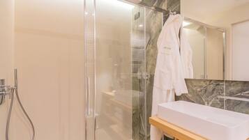 A modern bathroom with a glass-enclosed shower, a white sink, and a marble backsplash.