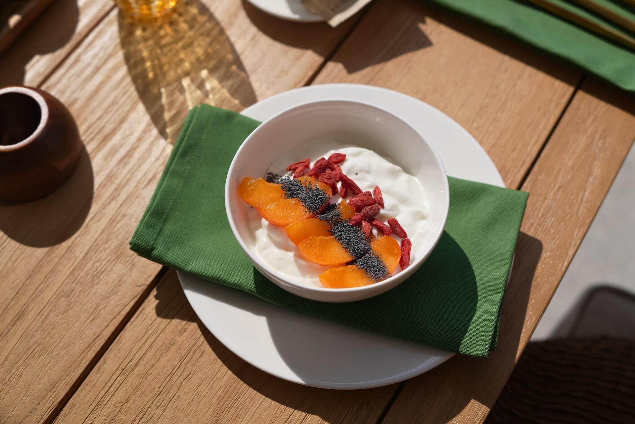 A bowl of yogurt topped with fruit and seeds on a wooden table.