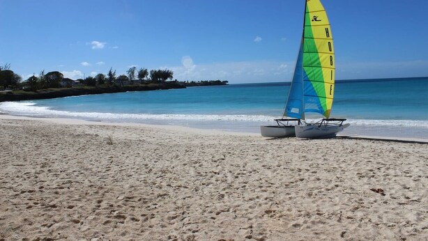 Una playa con un velero y aguas turquesas tranquilas.