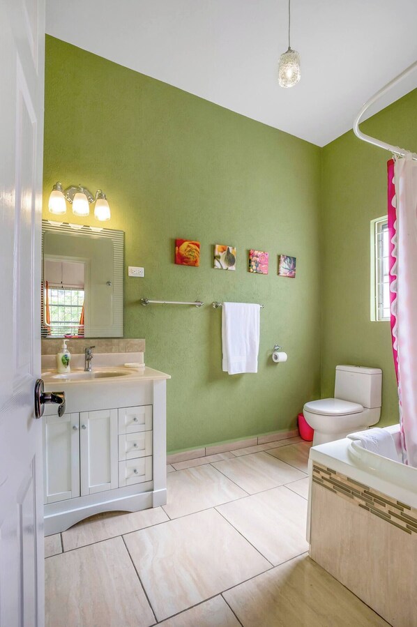 Un baño con pared verde, lavamanos blanco, espejo, toallero, inodoro y cortina de ducha.