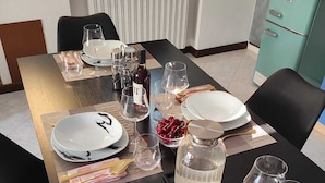 Une table à manger dressée avec des assiettes, des verres et des couverts, avec un radiateur et un meuble bleu-vert en arrière-plan.
