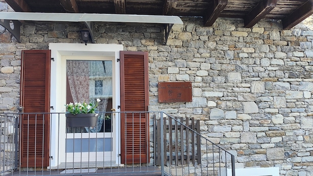 Un bâtiment en pierre avec un balcon en bois, une plante en pot et une enseigne.