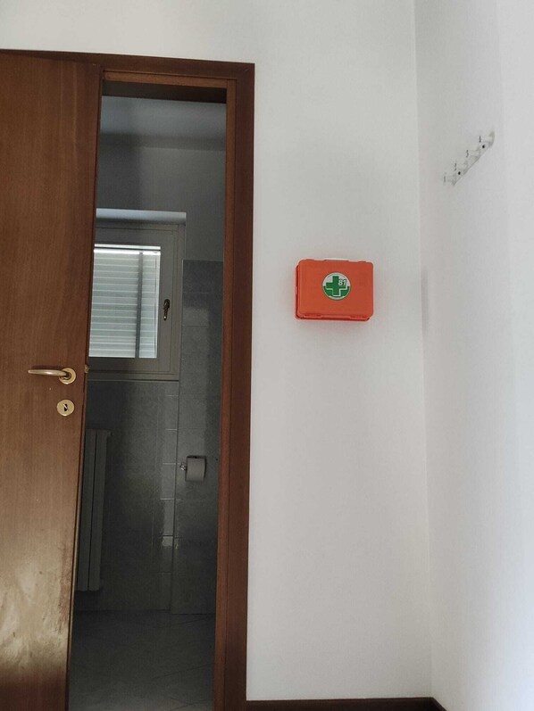 A room with a wooden door, a small red medical kit on the wall, and a window with blinds. - Keila Holiday Home – Mountains, Peace & WiFi (Colorina)