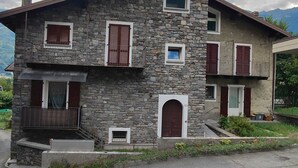 Une maison en pierre à deux étages, dotée d’un balcon, d’un petit porche et d’une porte surmontée d’une fenêtre.