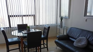 A modern living room with a dining area, featuring a round glass table, leather sofa, and a large window with blinds. - Lovely condo with AC in vibrant Tijuana Excellent location main avenue SAFE (Tijuana)