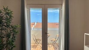 A room with a sliding glass door leading to a balcony with two chairs and a table. - Morgado Group - Quinta do Morgado - Morgado Privilege (Tavira)