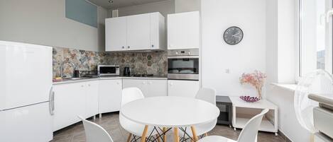 A modern kitchen with white cabinets, a round dining table, and a clock on the wall.