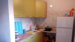 A compact kitchen with yellow cabinets, a white refrigerator, and a marble backsplash.