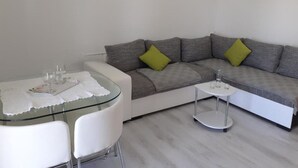 A modern living room with a grey sofa, two white chairs, a glass coffee table, and a small side table.